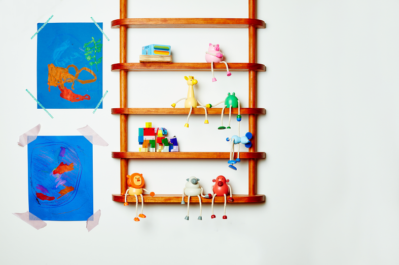 Drewniana figurka żyrafa na półce obok innych kolorowych drewnianych figurek na białej ścianie