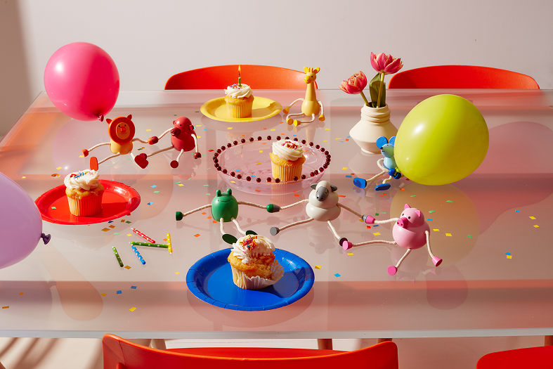 Kolorowe babeczki na talerzach obok drewnianej figurki żyrafa i balonów na stole