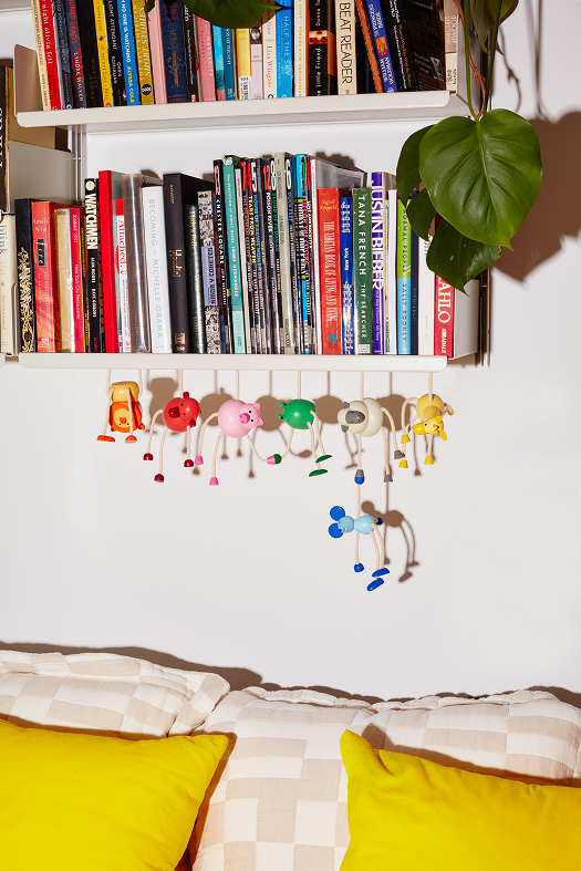 Kolorowe drewniane figurki zwierząt, w tym drewniana figurka żyrafa, wiszące pod półką z książkami