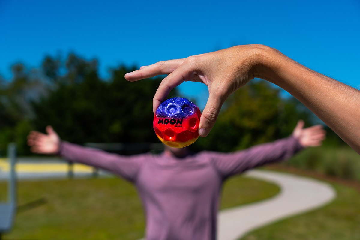 Piłeczka Waboba Gradient Moon Ball trzymana w dłoni na tle rozmytej osoby na zewnątrz