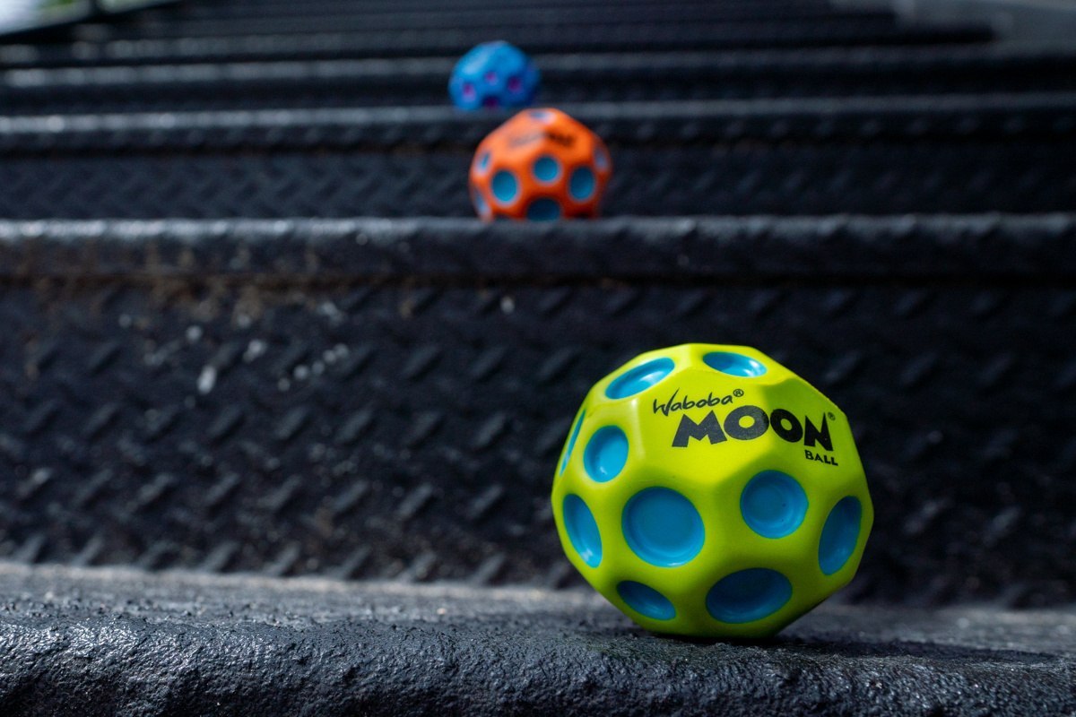 Zielona piłeczka Moon Ball Waboba z niebieskimi otworami na metalowych schodach
