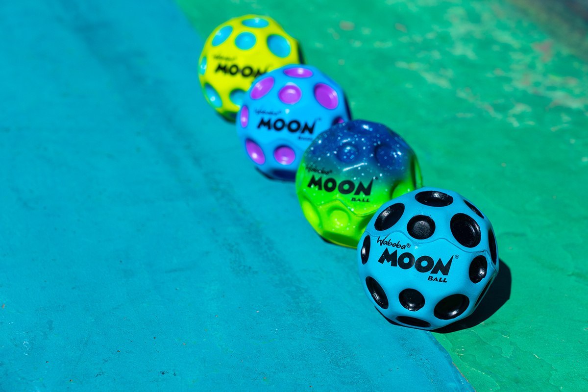 Kolorowe piłeczki Moon Ball Waboba ułożone na niebiesko-zielonym tle do zabawy na świeżym powietrzu