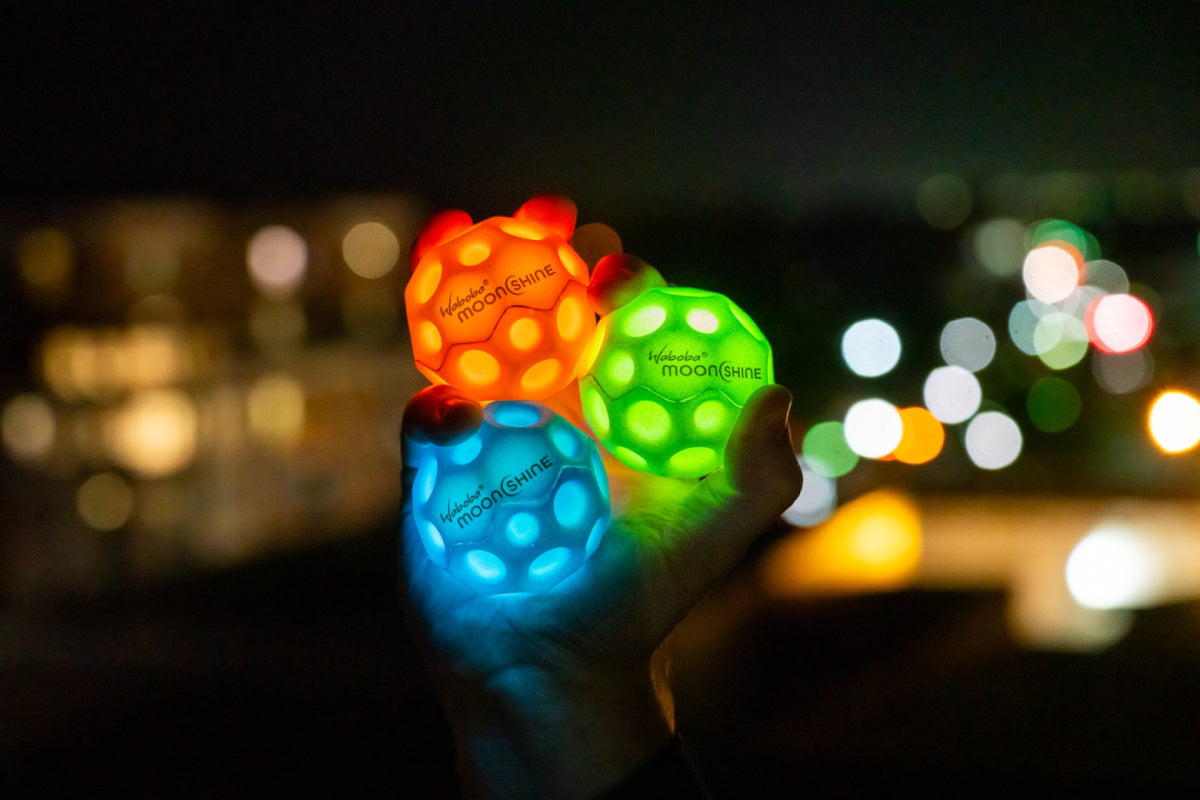 Piłeczka świecąca Waboba Moonshine w trzech kolorach trzymana w dłoni nocą na tle rozmytych świateł miasta