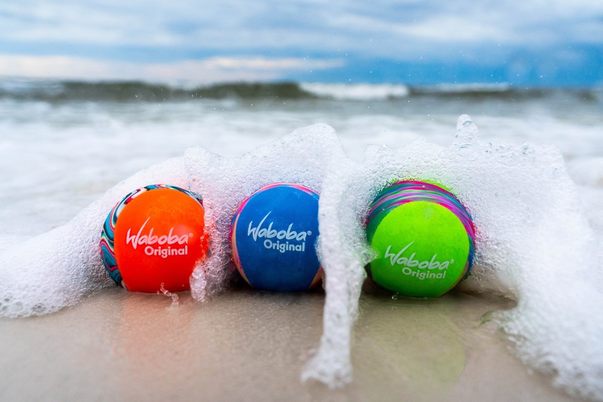 Piłeczka Waboba Original w trzech kolorach na plaży z falami rozbijającymi się o piasek