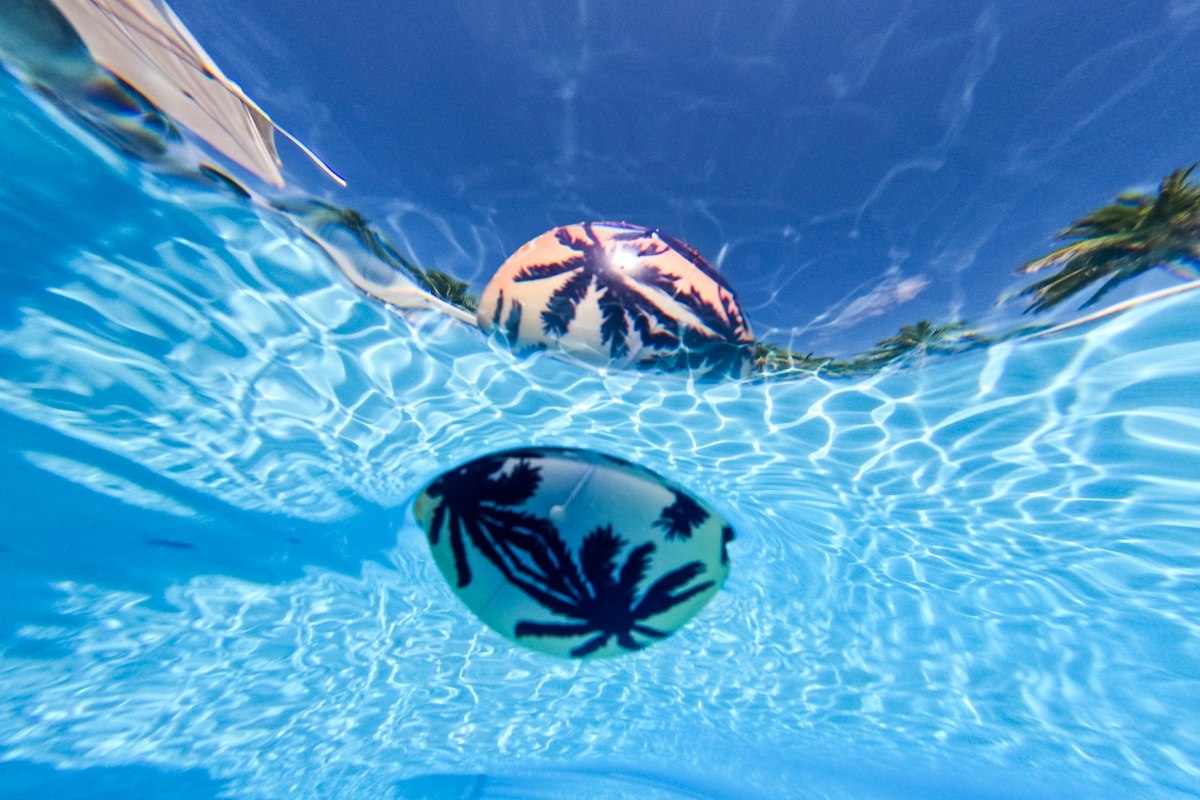 Piłka na wodę Waboba Tropical Kahuna z motywem palm, unosząca się na powierzchni basenu pod niebieskim niebem