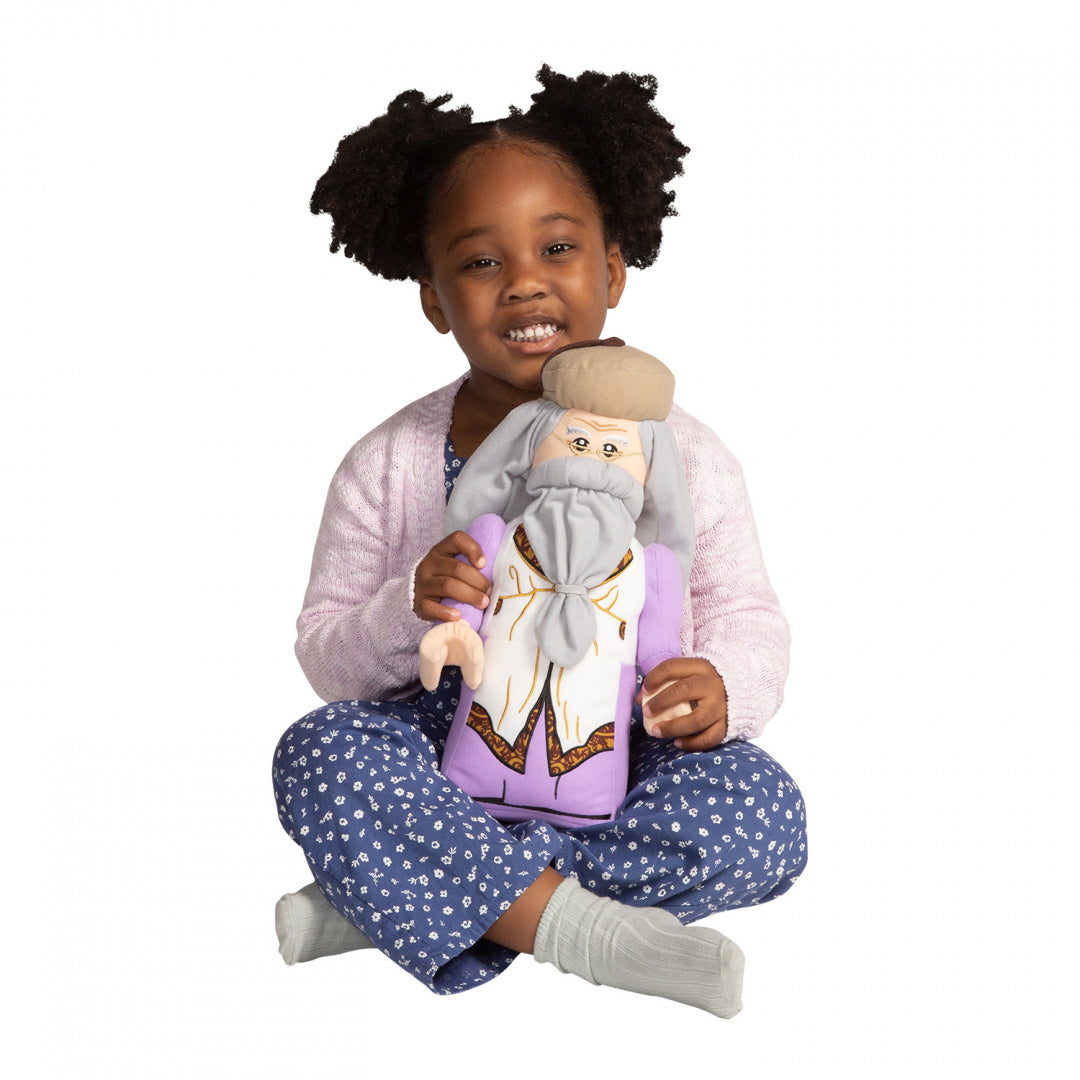 Mała dziewczynka siedzi i trzyma pluszaka Dumbledore LEGO Harry Potter w fioletowym stroju