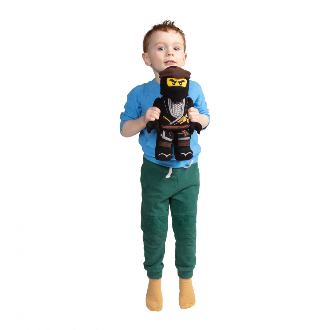 Chłopiec trzyma pluszak LEGO Ninjago Cole czarnego ninja z żółtymi oczami i brązową opaską
