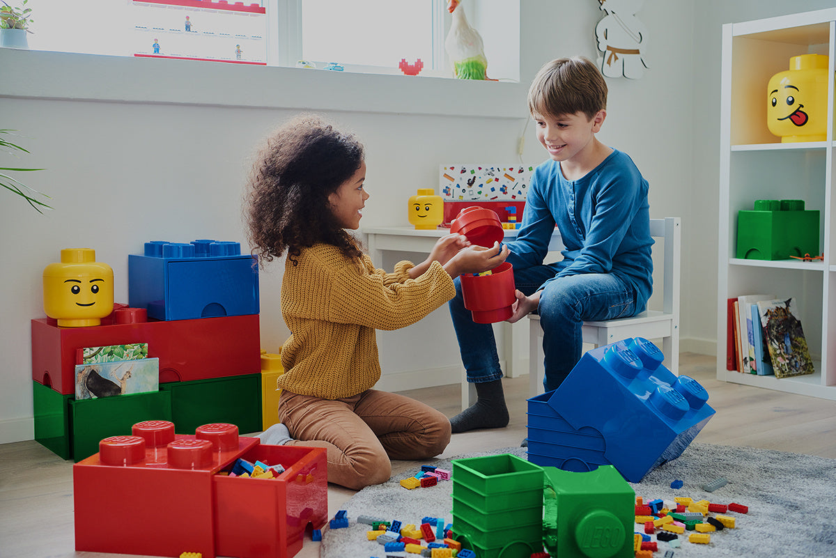 Dzieci bawiące się pojemnikiem LEGO zielonym i innymi kolorowymi pojemnikami w kształcie klocków LEGO