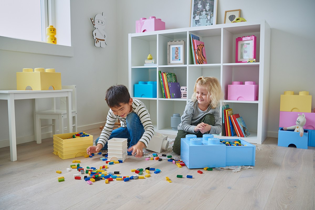 Dzieci bawiące się klockami obok pojemnika LEGO na klocki w jasnym pokoju zabaw