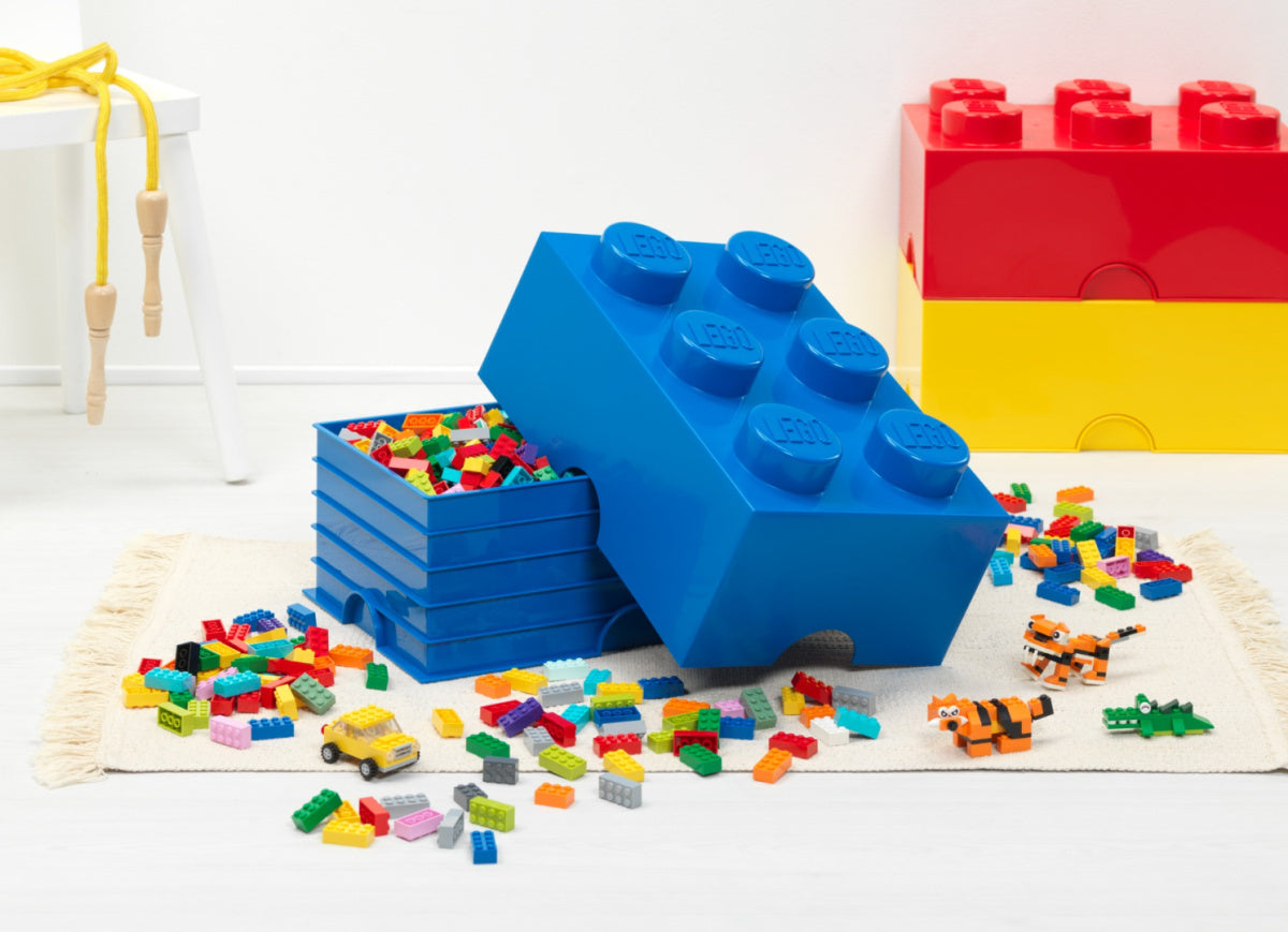 Pojemnik LEGO na zabawki w kształcie niebieskiej klockowej kostki z rozsypanymi kolorowymi klockami LEGO