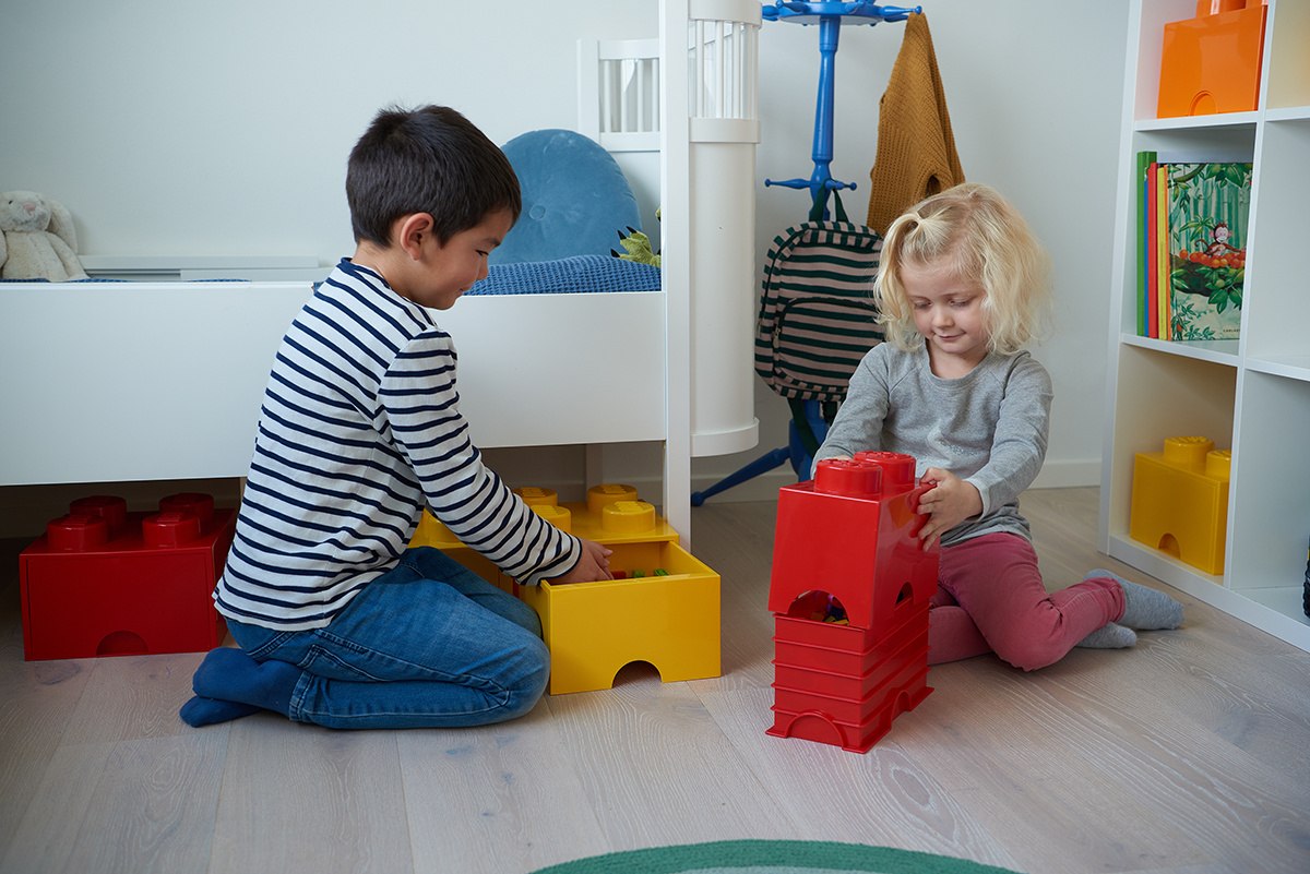 Dzieci bawiące się pojemnikami LEGO, w tym pojemnik LEGO czerwony, w jasnym pokoju dziecięcym