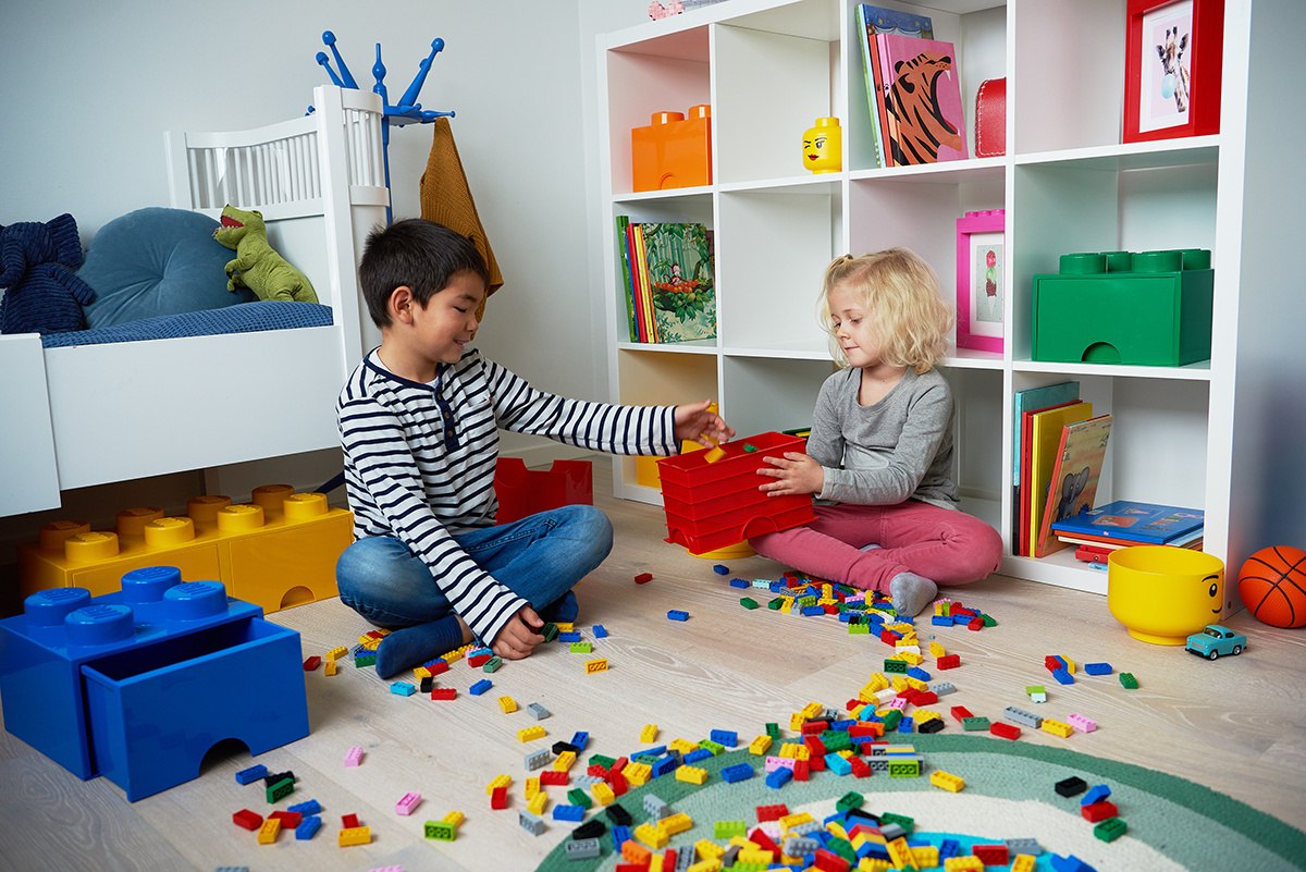 Dzieci bawią się klockami LEGO z czerwonym pojemnikiem LEGO czerwonym na podłodze w pokoju dziecięcym