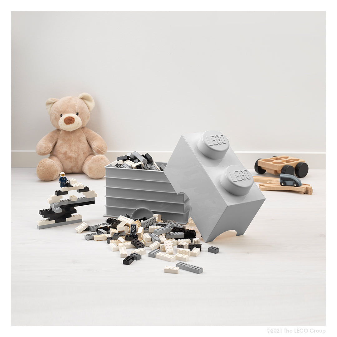 Szary pojemnik LEGO Brick szary w formie dużej klocka z rozsypanymi czarno-białymi klockami LEGO obok pluszowego misia