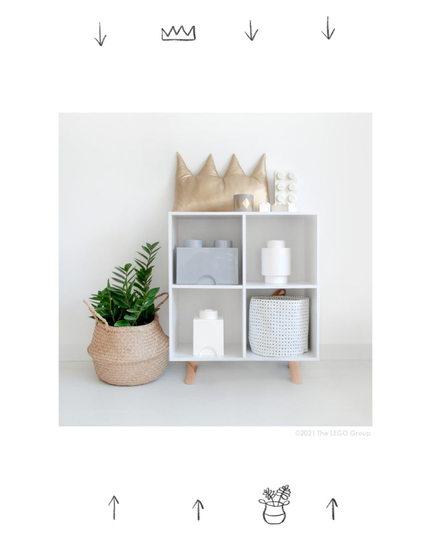 Pojemnik LEGO Brick szary w białej szafce obok zielonej rośliny w wiklinowym koszu