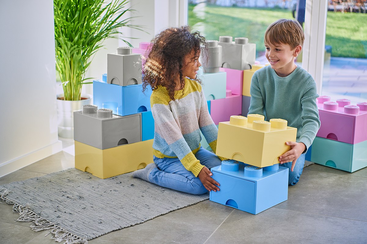 Dzieci bawiące się pojemnikiem LEGO jasnoniebieskim w kształcie dużej klocka do przechowywania z innymi kolorowymi pojemnikami