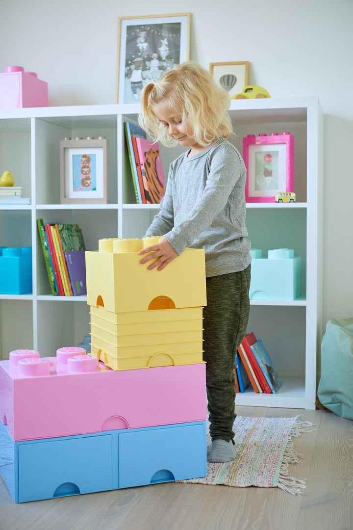Dziecko bawiące się pojemnikiem LEGO Brick 8 jasnoróżowy w pokoju dziecięcym z innymi kolorowymi pojemnikami