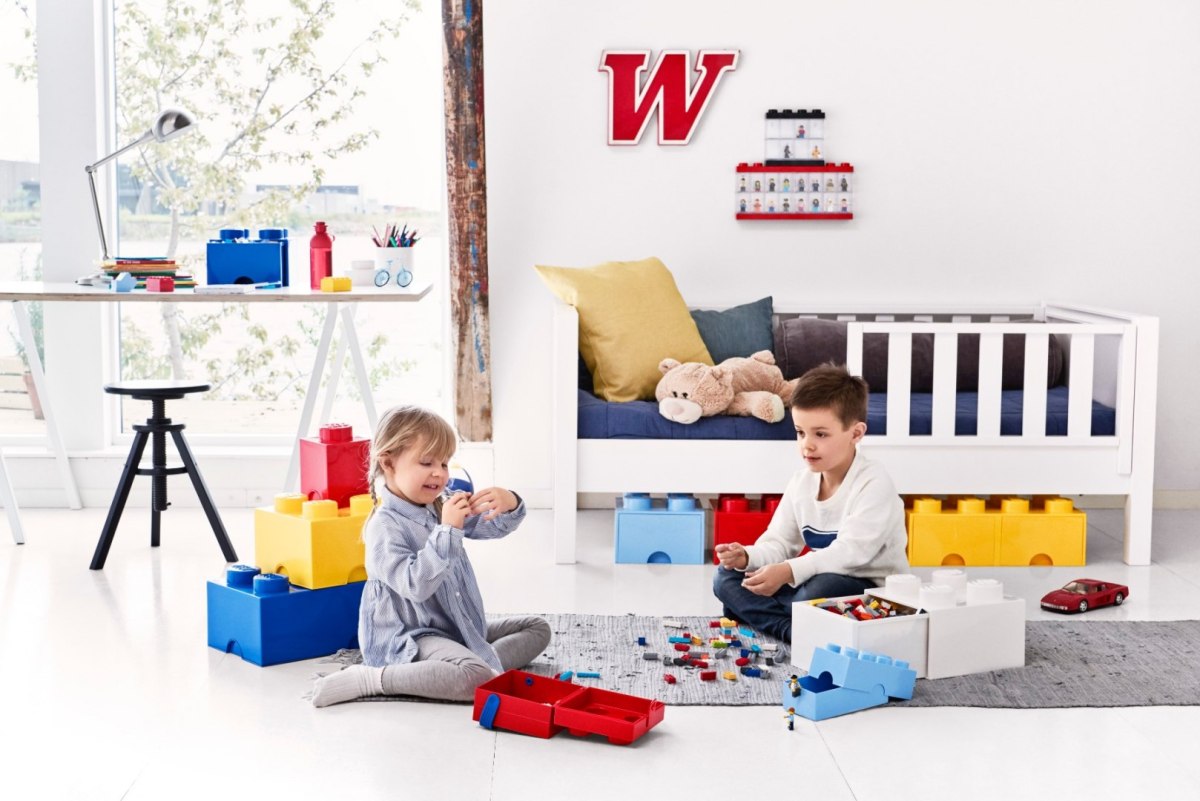 Dzieci bawiące się z pojemnikiem LEGO na zabawki w kształcie klocków w jasnym pokoju dziecięcym