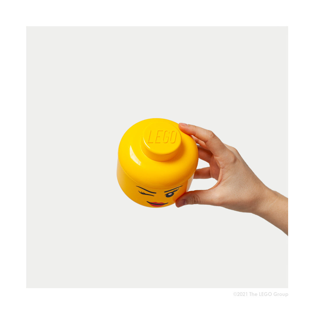 Pojemnik LEGO głowa dziewczynka w żółtym kolorze trzymany w dłoni na białym tle