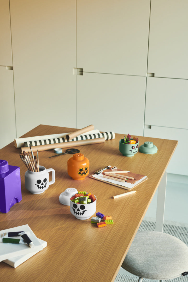 Pojemnik LEGO głowa szkieletor w formie kubka na biurku z artykułami plastycznymi i klockami LEGO