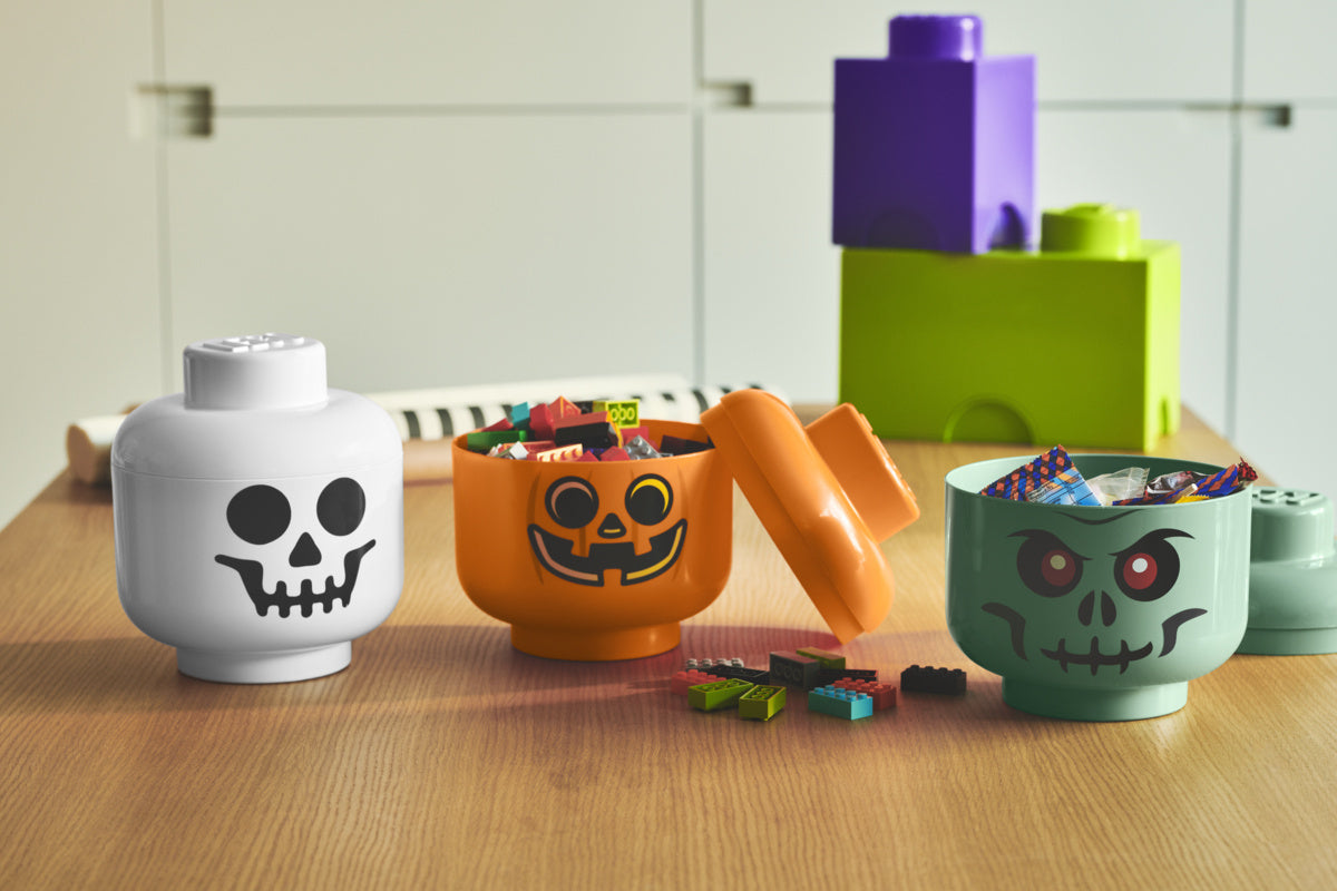 Pojemnik LEGO głowa zombie w zielonym kolorze z cukierkami i klockami na drewnianym stole