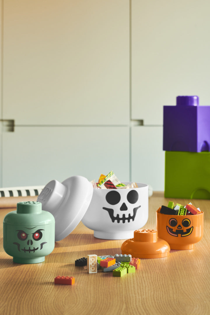 Pojemnik LEGO głowa zombie w zielonym, białym i pomarańczowym kolorze z pokrywkami i klockami na stole