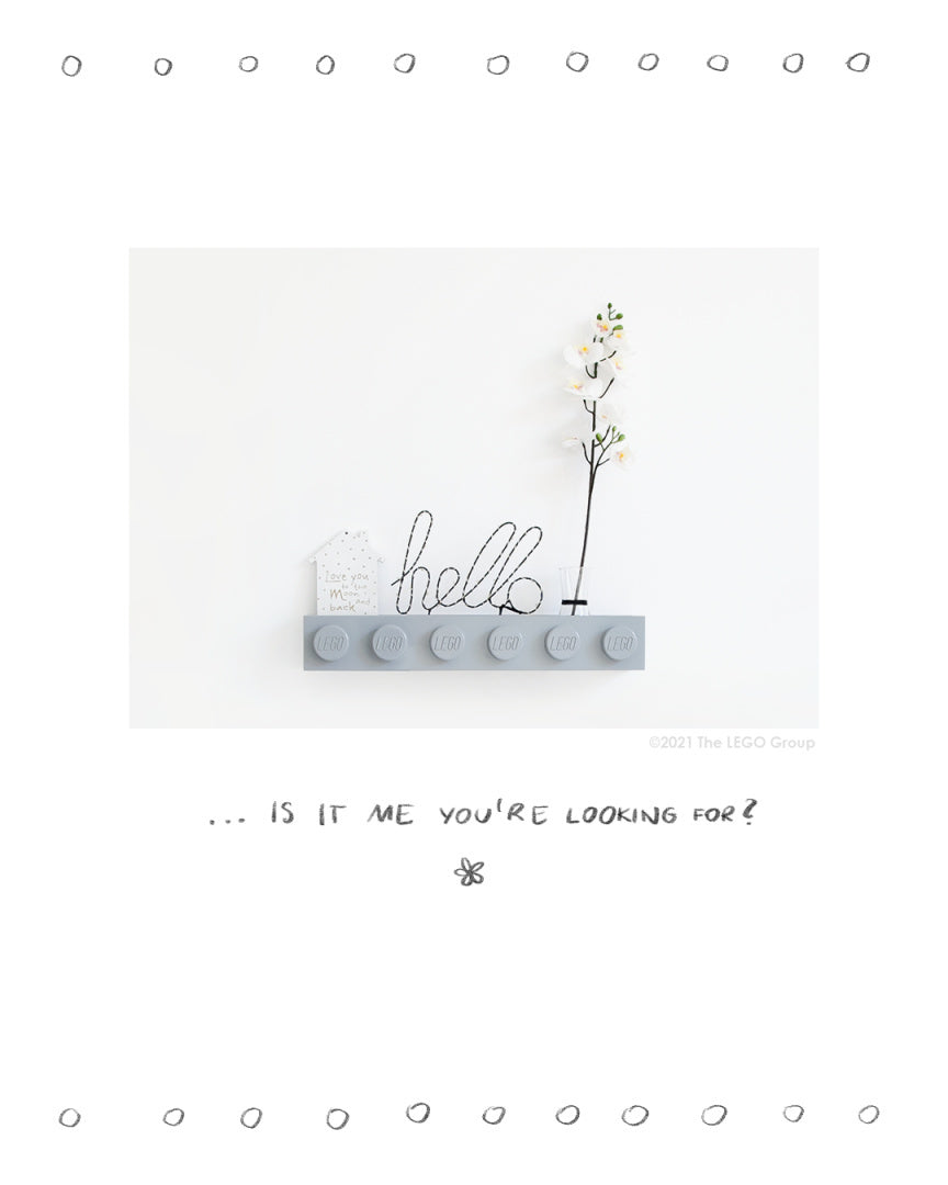 Szara półka LEGO zamontowana na ścianie z dekoracyjnymi przedmiotami i kwiatem