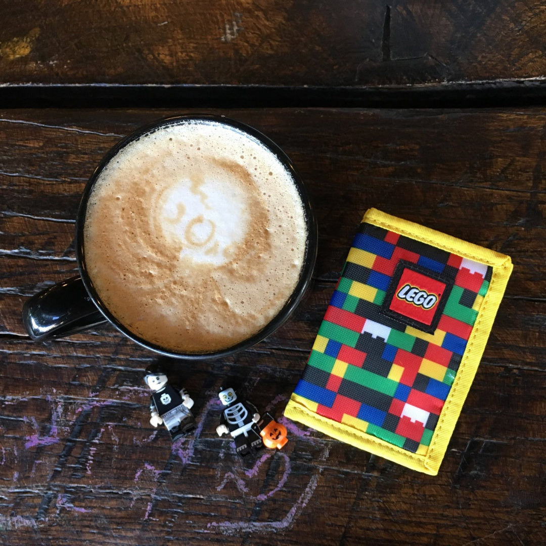 Kolorowy portfel LEGO dla dzieci z motywem klocków obok filiżanki kawy i figurek na drewnianym stole