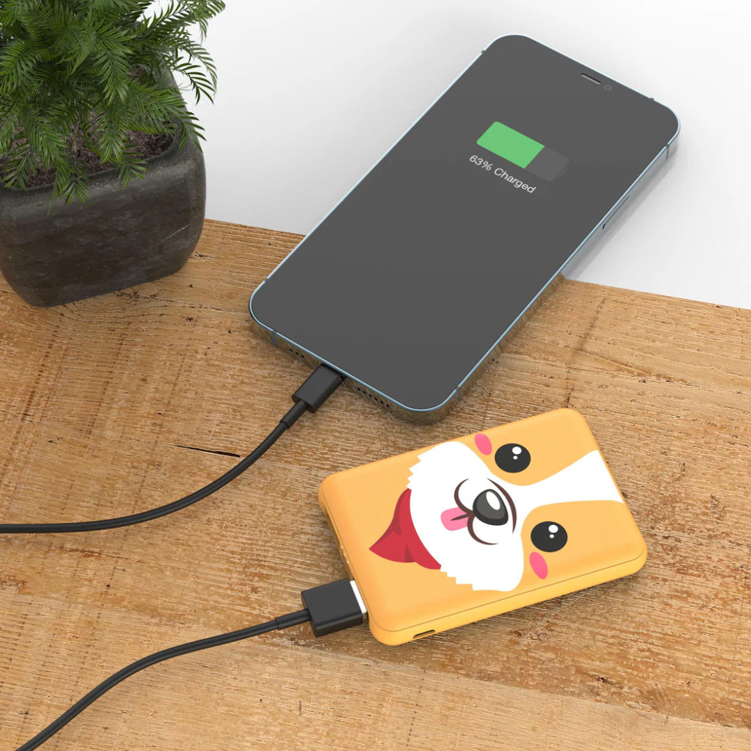 Powerbank piesek corgi marki Yamann z uroczym wzorem psa podłączony do smartfona na drewnianym stole