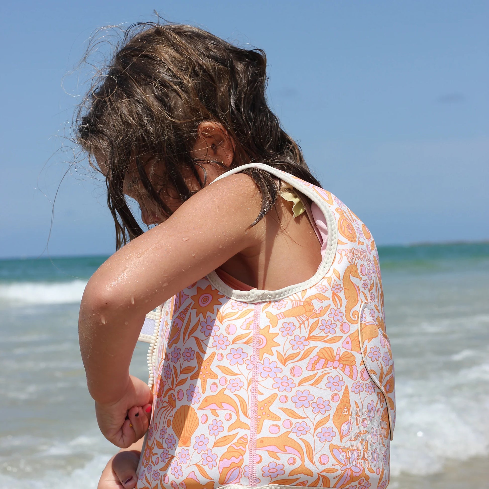 Dziewczynka nosząca kolorową kamizelkę do pływania dla dzieci nad morzem