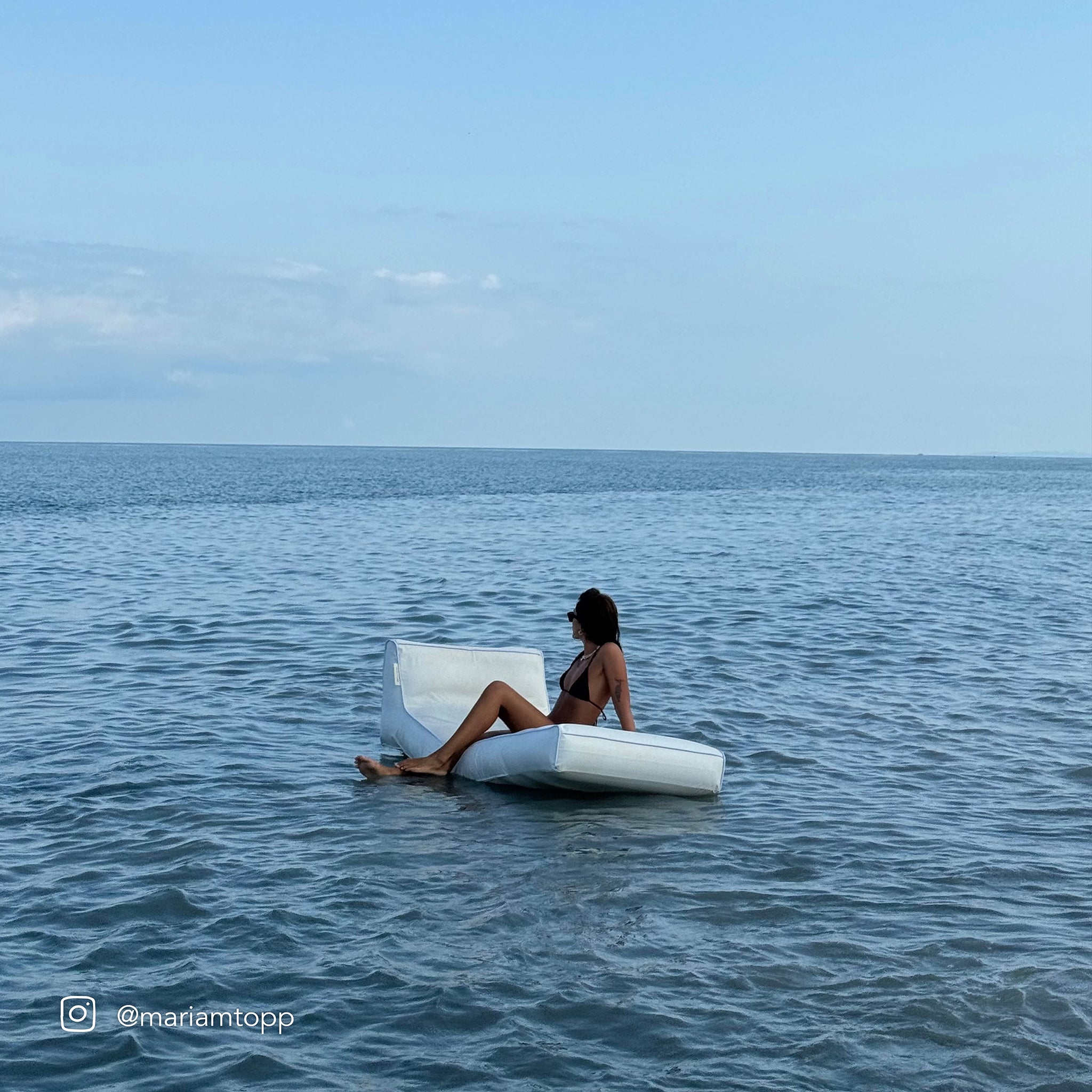 Luksusowy materac do leżenia SUNNY LIFE z siedzącą kobietą na wodzie przy słonecznym niebie