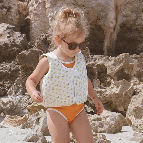 Kamizelka do pływania dla dzieci SUNNY LIFE w jasne wzory na małej dziewczynce na plaży