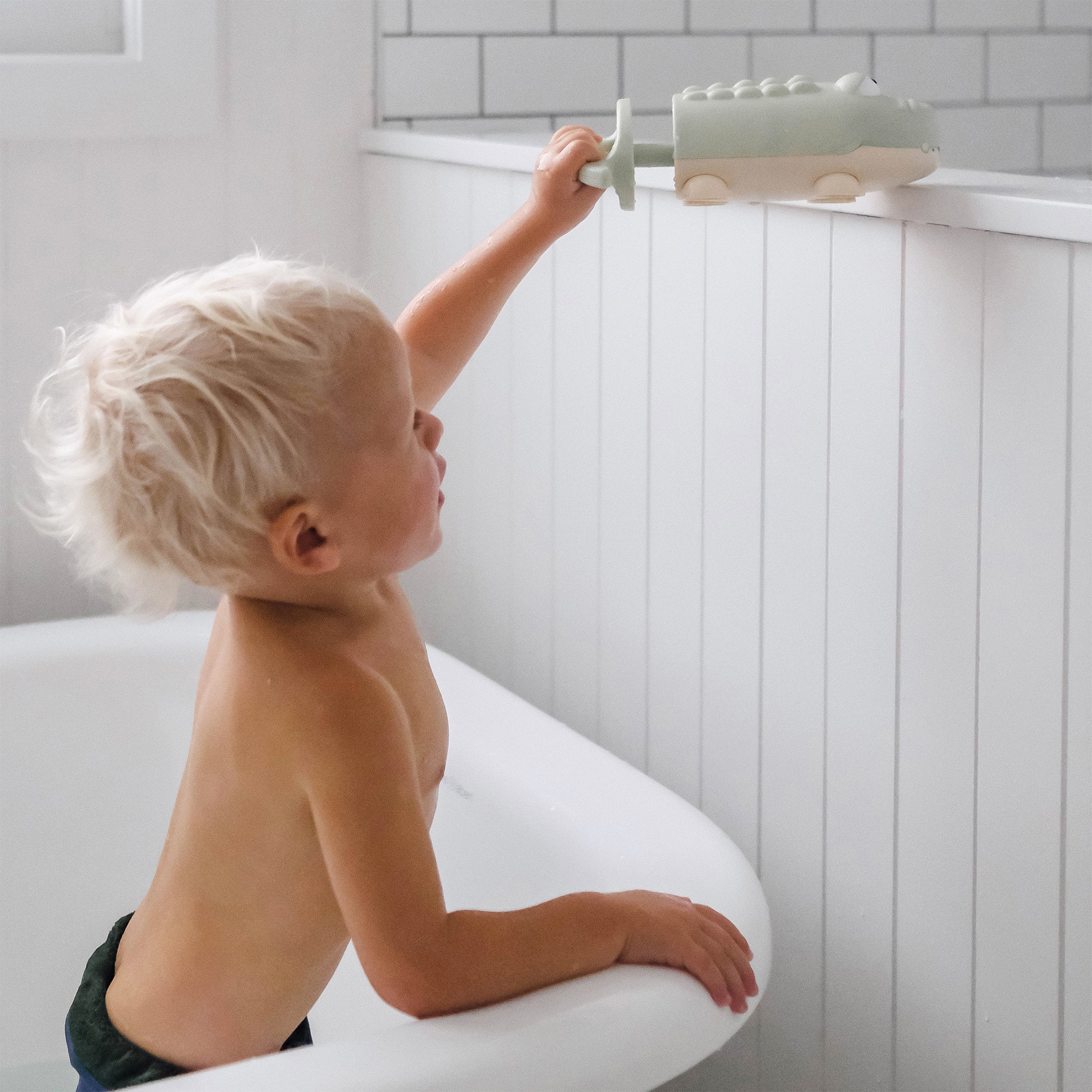 Małe dziecko bawiące się pistoletem wodnym dla dzieci krokodyl marki Sunny Life w łazience