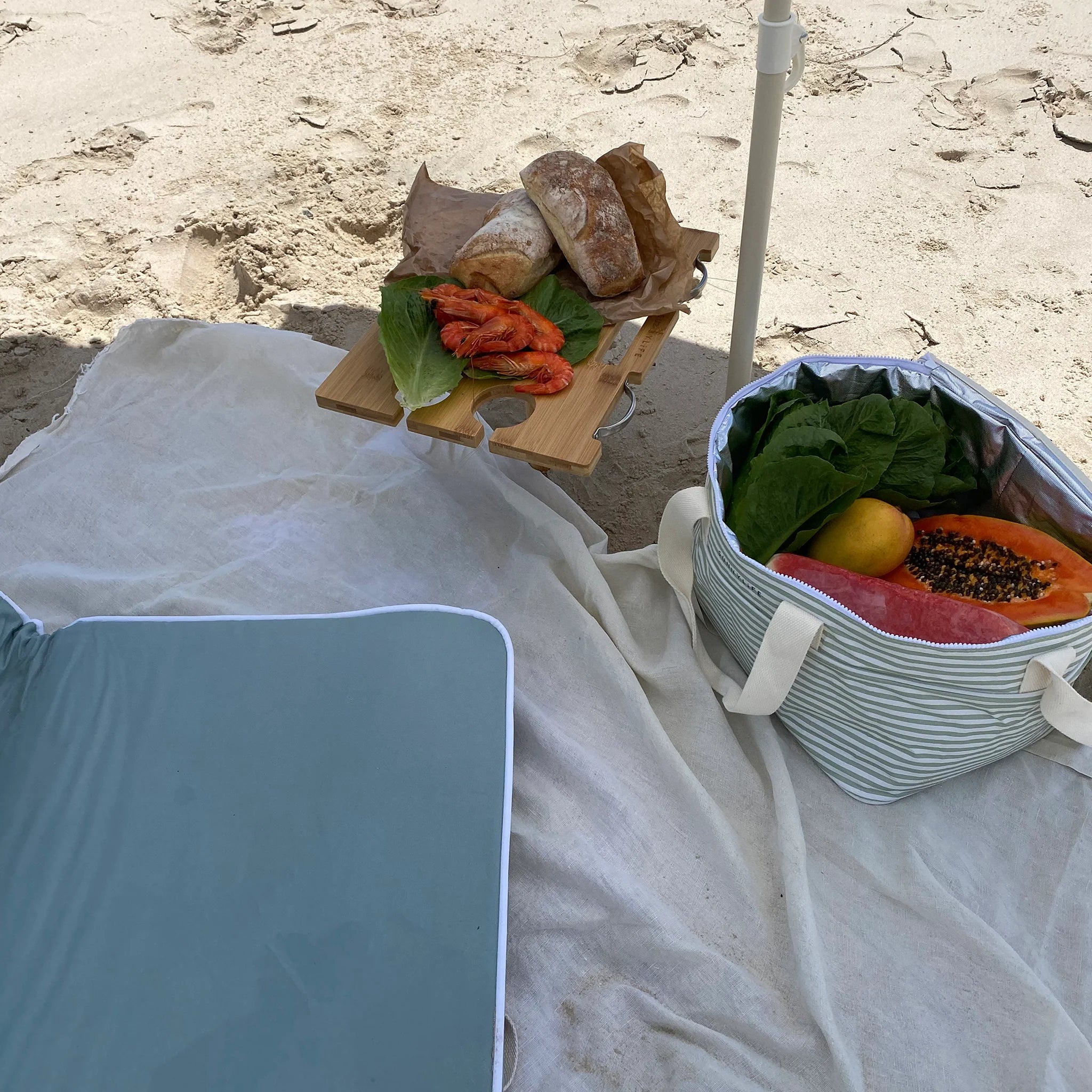 Przenośny stół piknikowy Sunny Life z jedzeniem na plaży na białym kocu