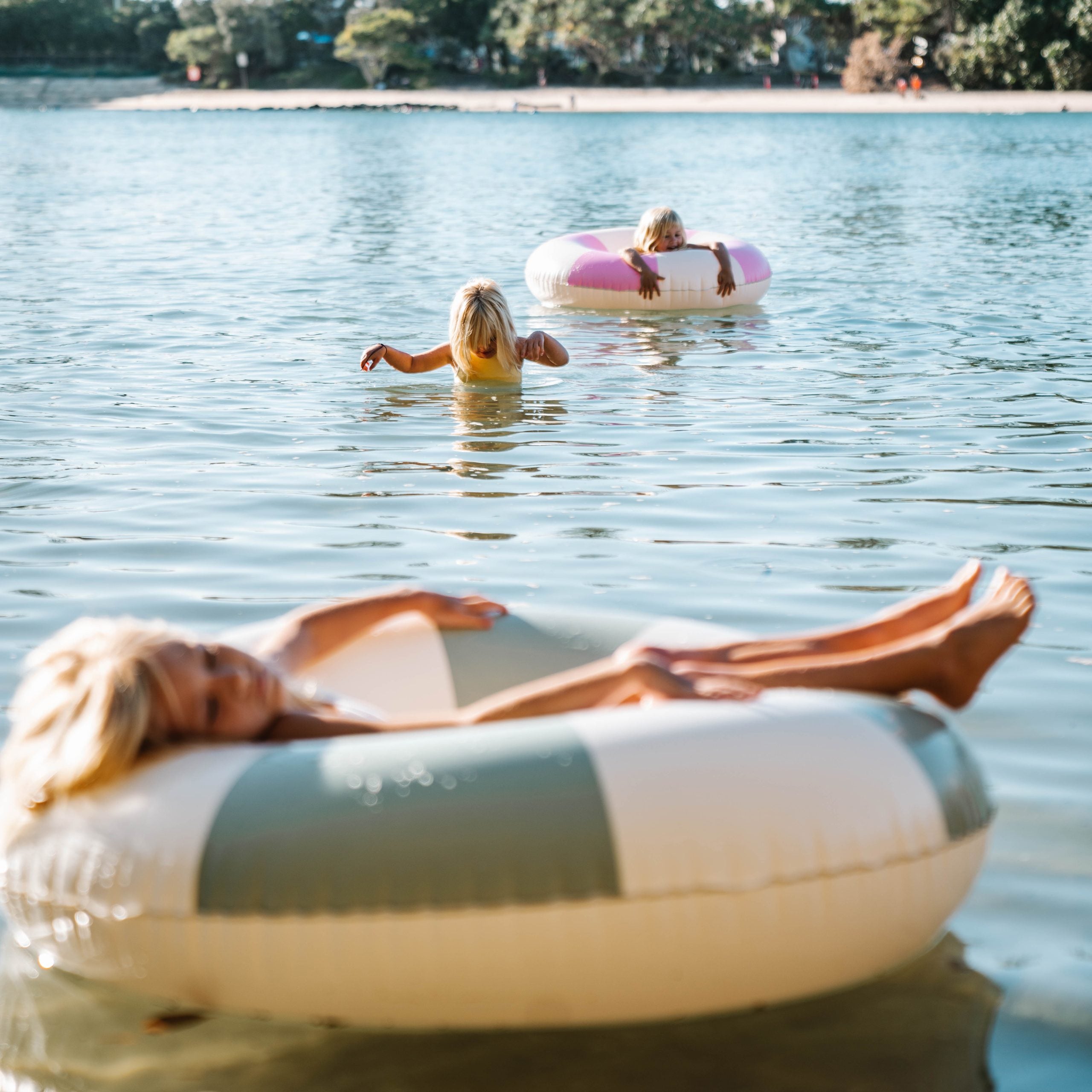 Koło do pływania dla dorosłych marki SUNNY LIFE używane przez osoby na jeziorze podczas słonecznego dnia