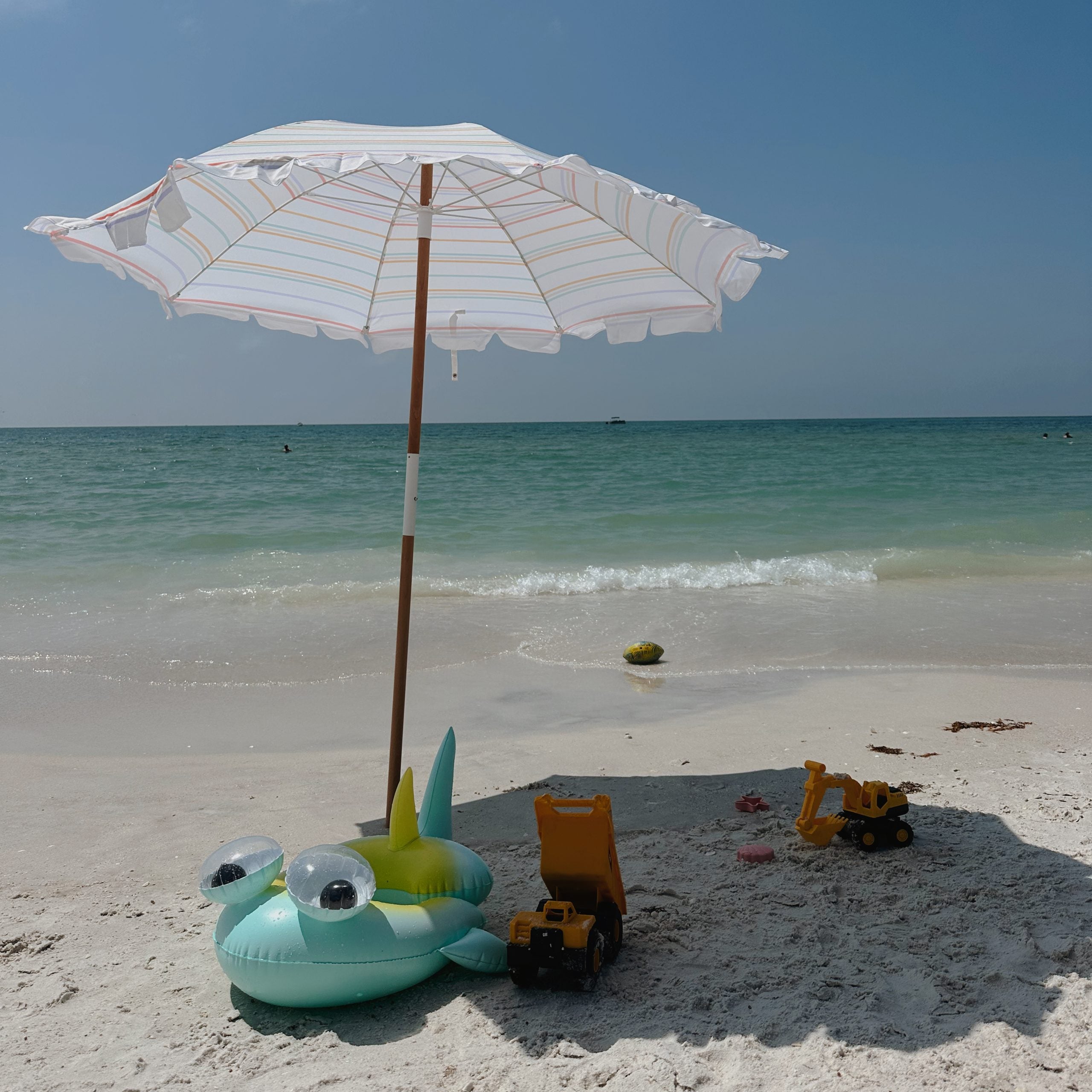 Koło do pływania dla dzieci w kształcie ryby na plaży pod parasolem przy morzu z zabawkami