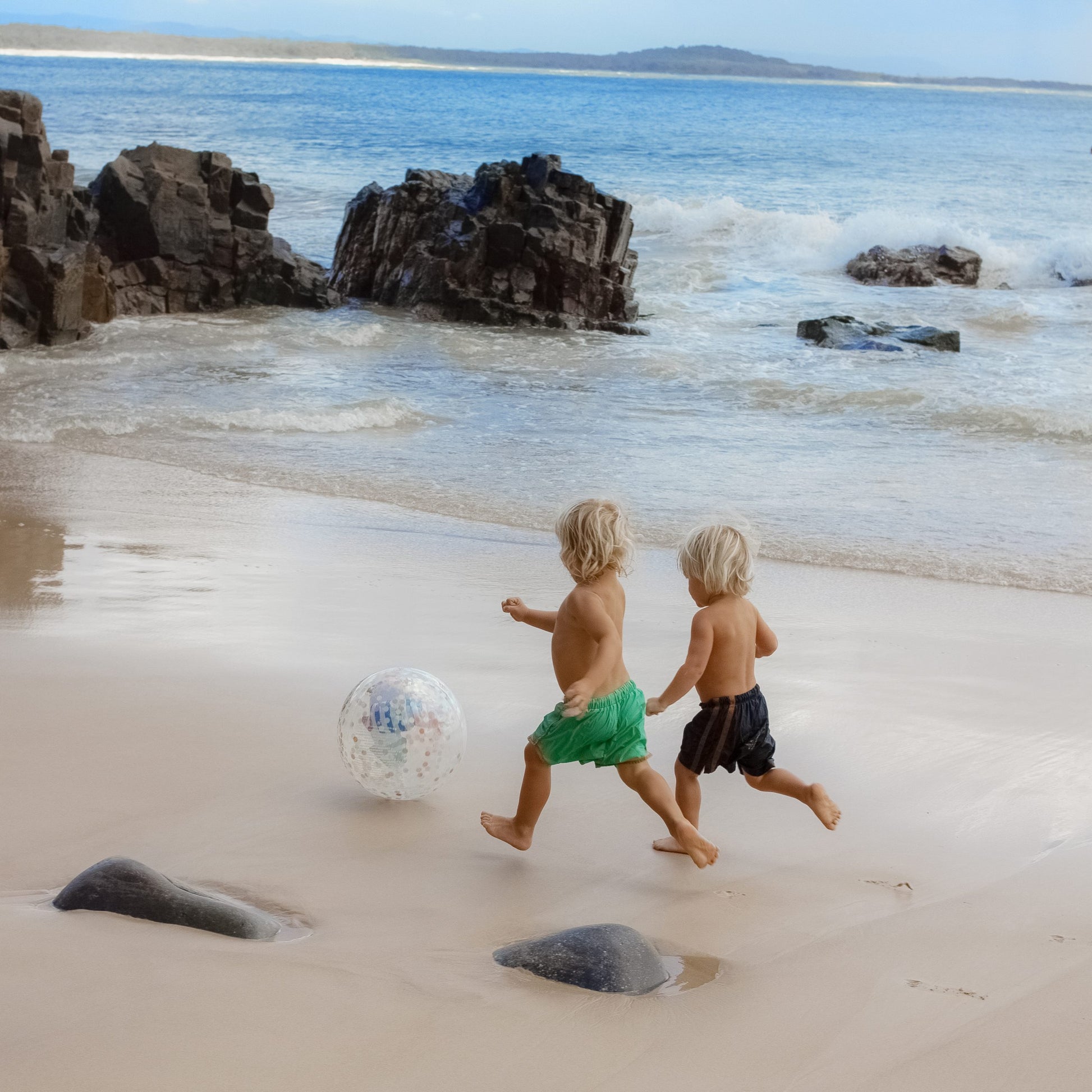 Dwoje dzieci bawi się na plaży nadmuchiwaną piłką plażową dla dzieci marki LOQI