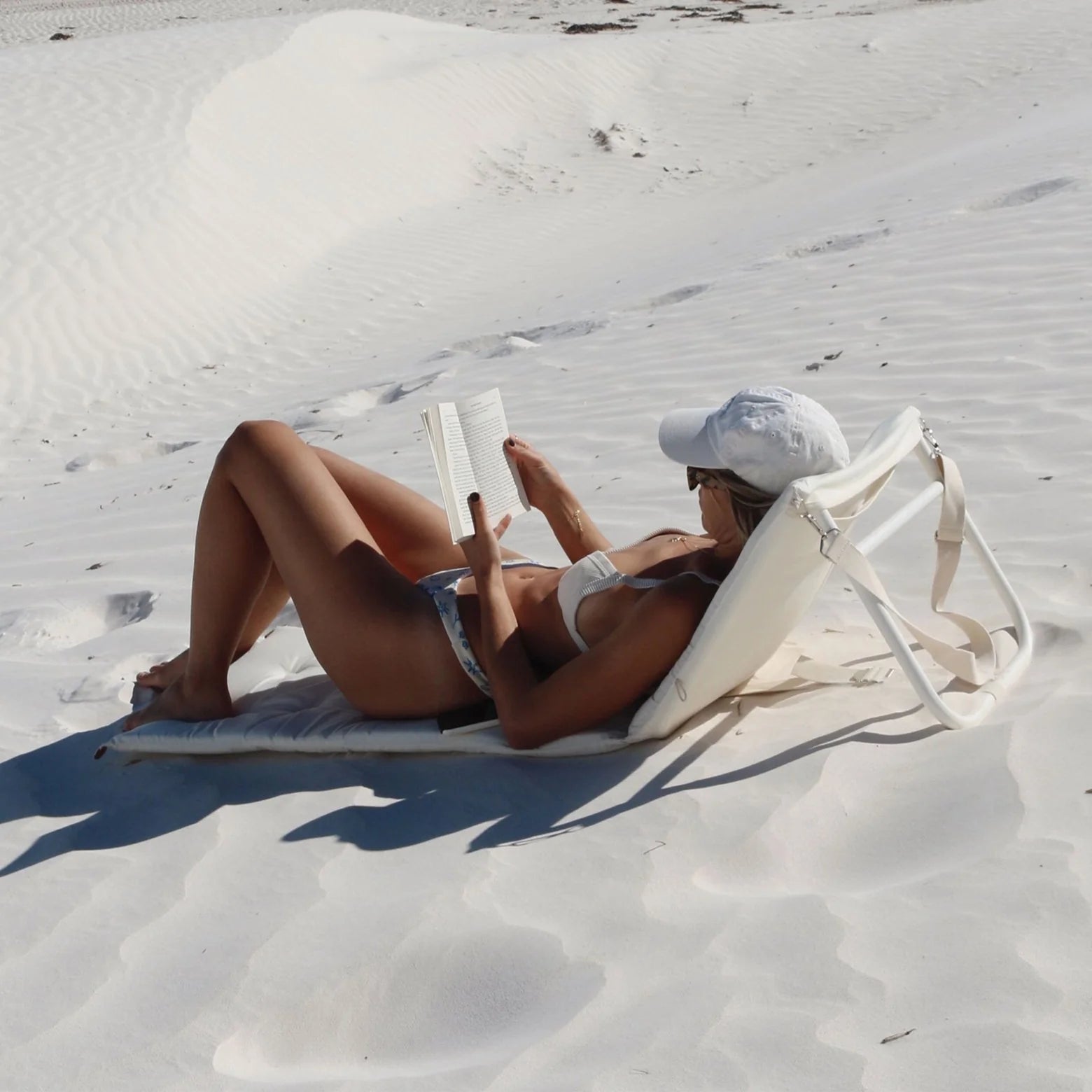 Kobieta odpoczywająca na białym rozkładanym leżaku plażowym Sunny Life na piasku