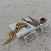 Biały rozkładany leżak plażowy Sunny Life z dzieckiem leżącym na piasku i żółtym ręcznikiem