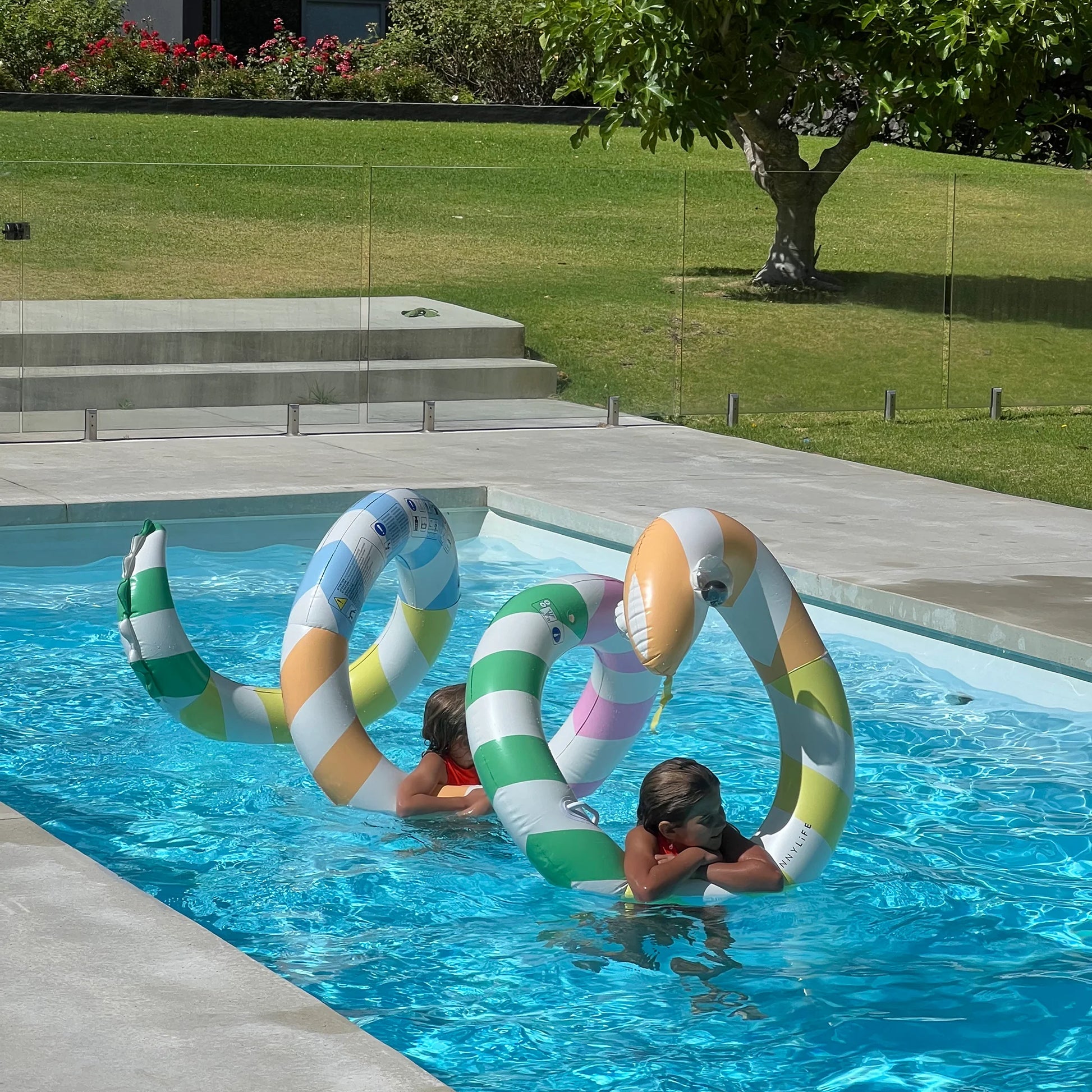 Gigantyczny dmuchany makaron LOQI w paski w basenie z dziećmi bawiącymi się latem