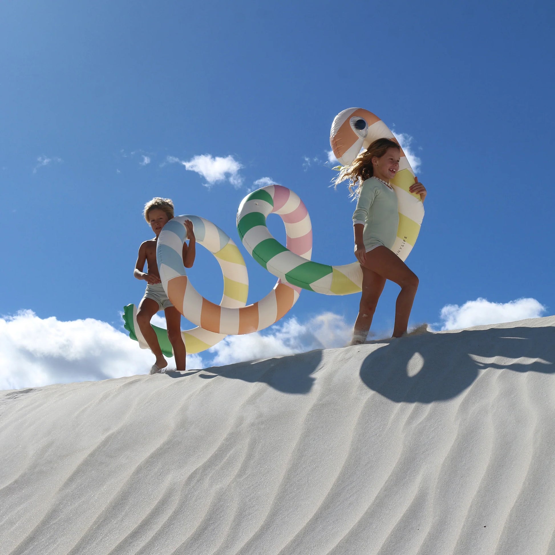 Dzieci bawiące się gigantycznym dmuchanym makaronem na plaży pod niebieskim niebem