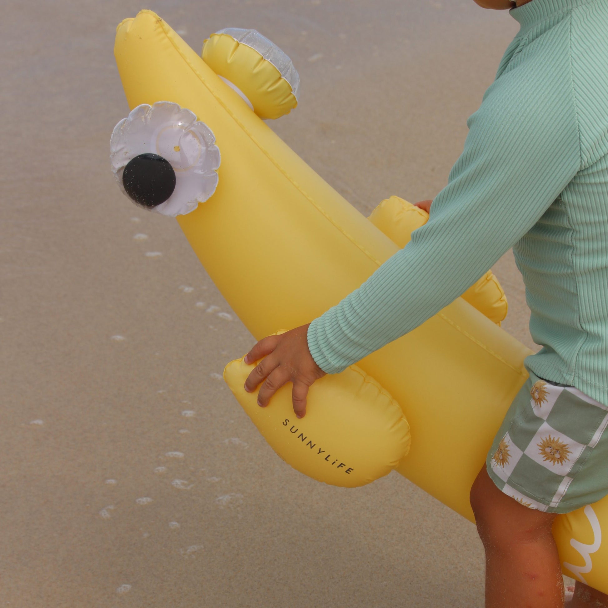 Dmuchane makarony do pływania dla dzieci w kształcie żółtego banana trzymane przez dziecko na plaży