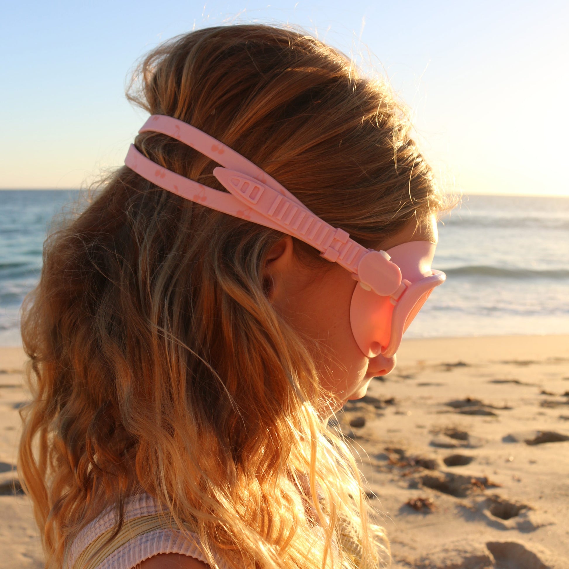 Różowa maska do pływania dla dzieci firmy LOQI na głowie dziewczynki na plaży o zachodzie słońca