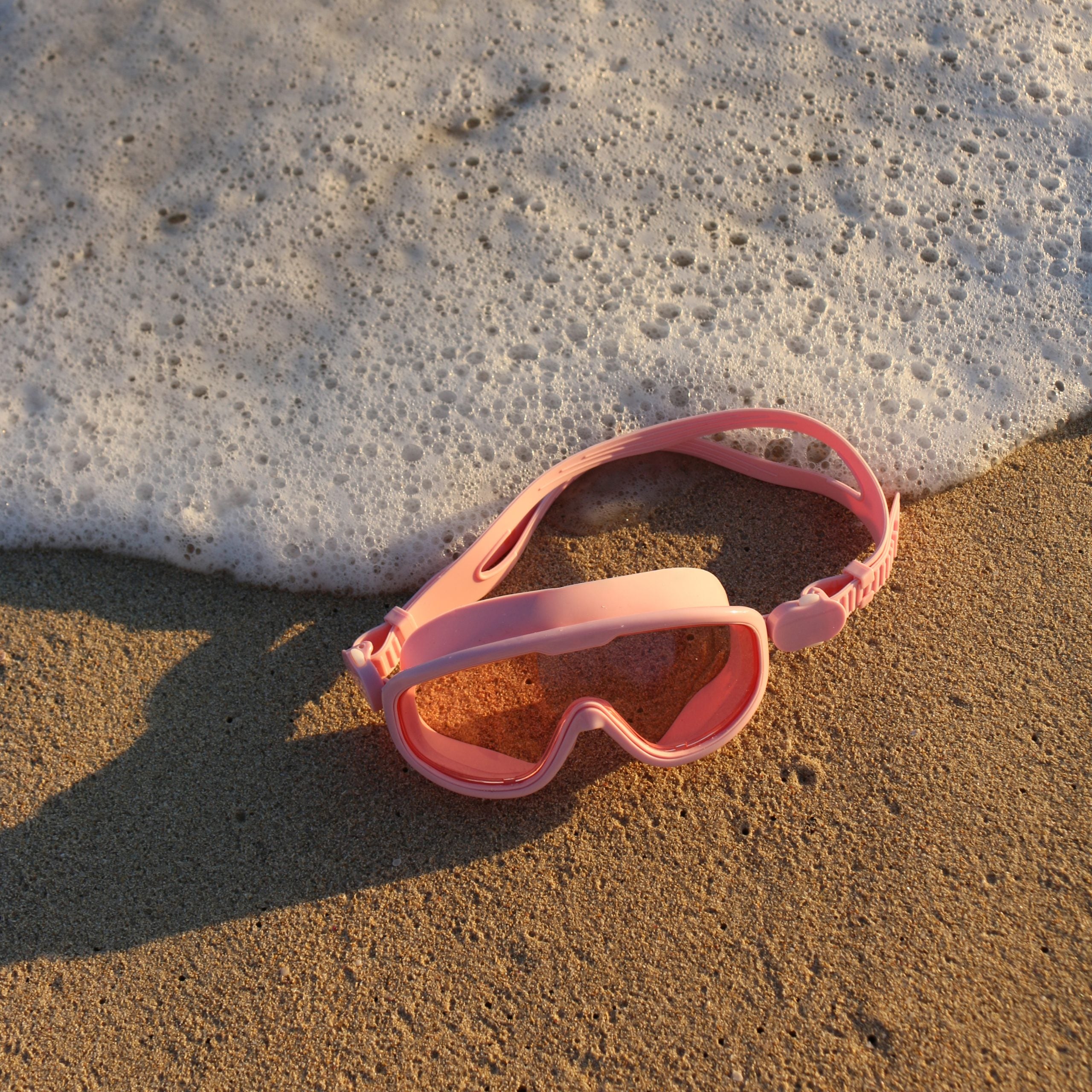 Różowa maska do pływania dla dzieci marki LOQI leżąca na piasku przy brzegu morza