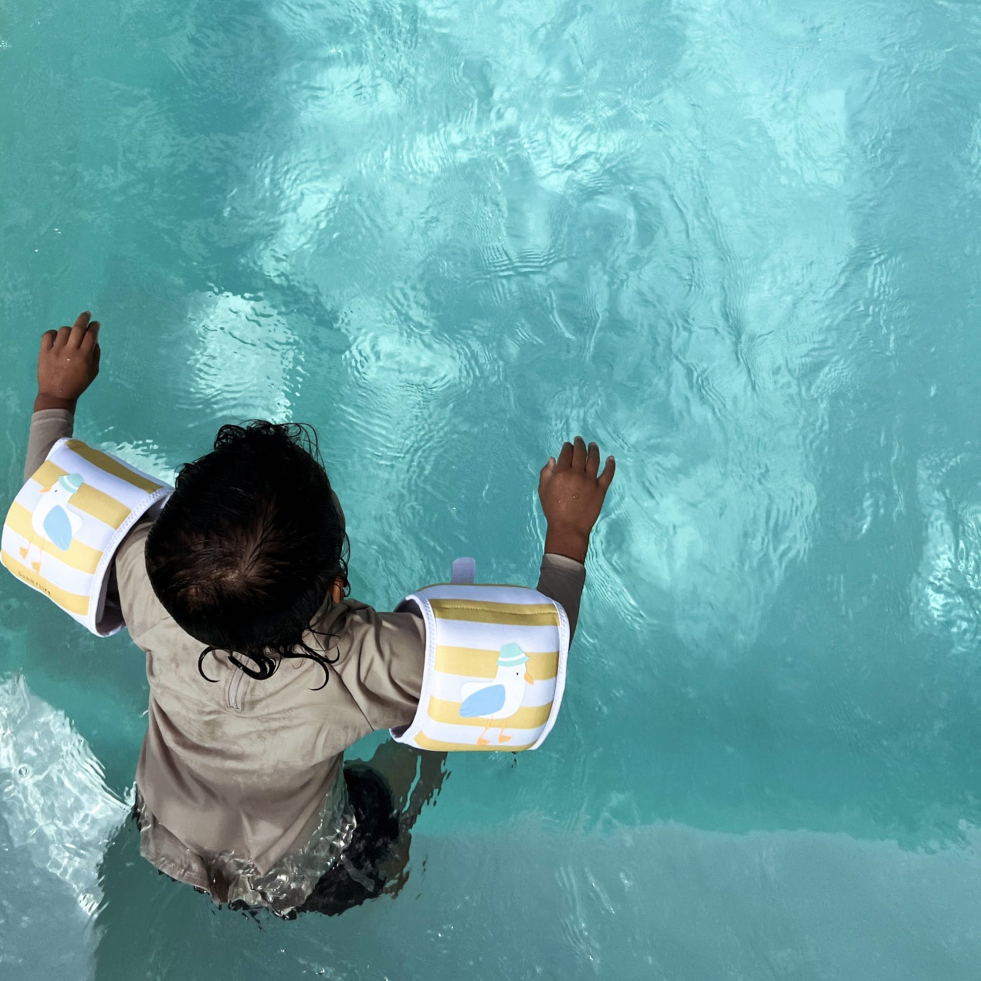 Dziecko pływające w basenie w kolorowych rękawkach do pływania dla dzieci marki LOQI