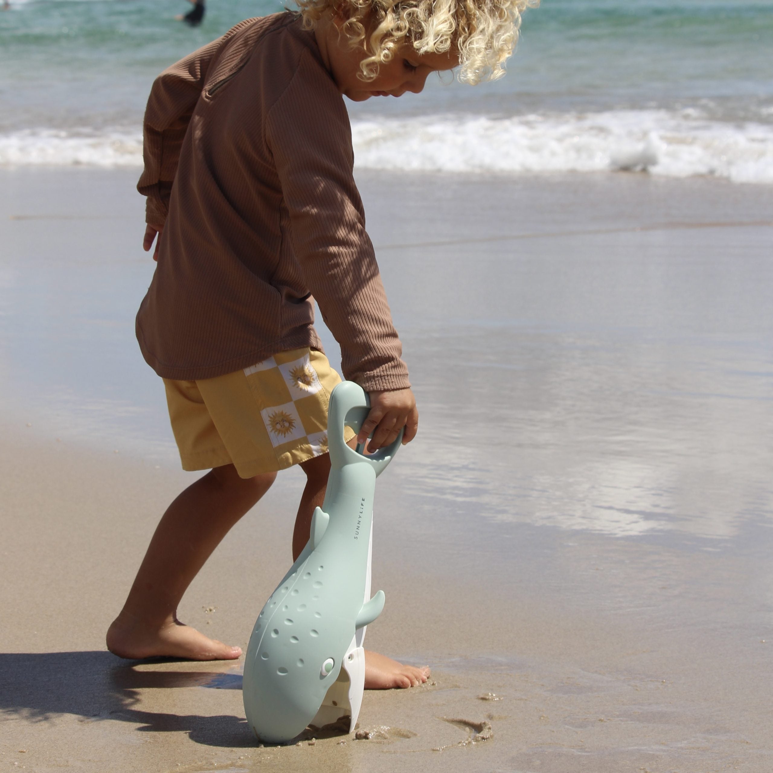 Łapki do piasku wieloryb marki LOQI trzymane przez dziecko na plaży przy morzu