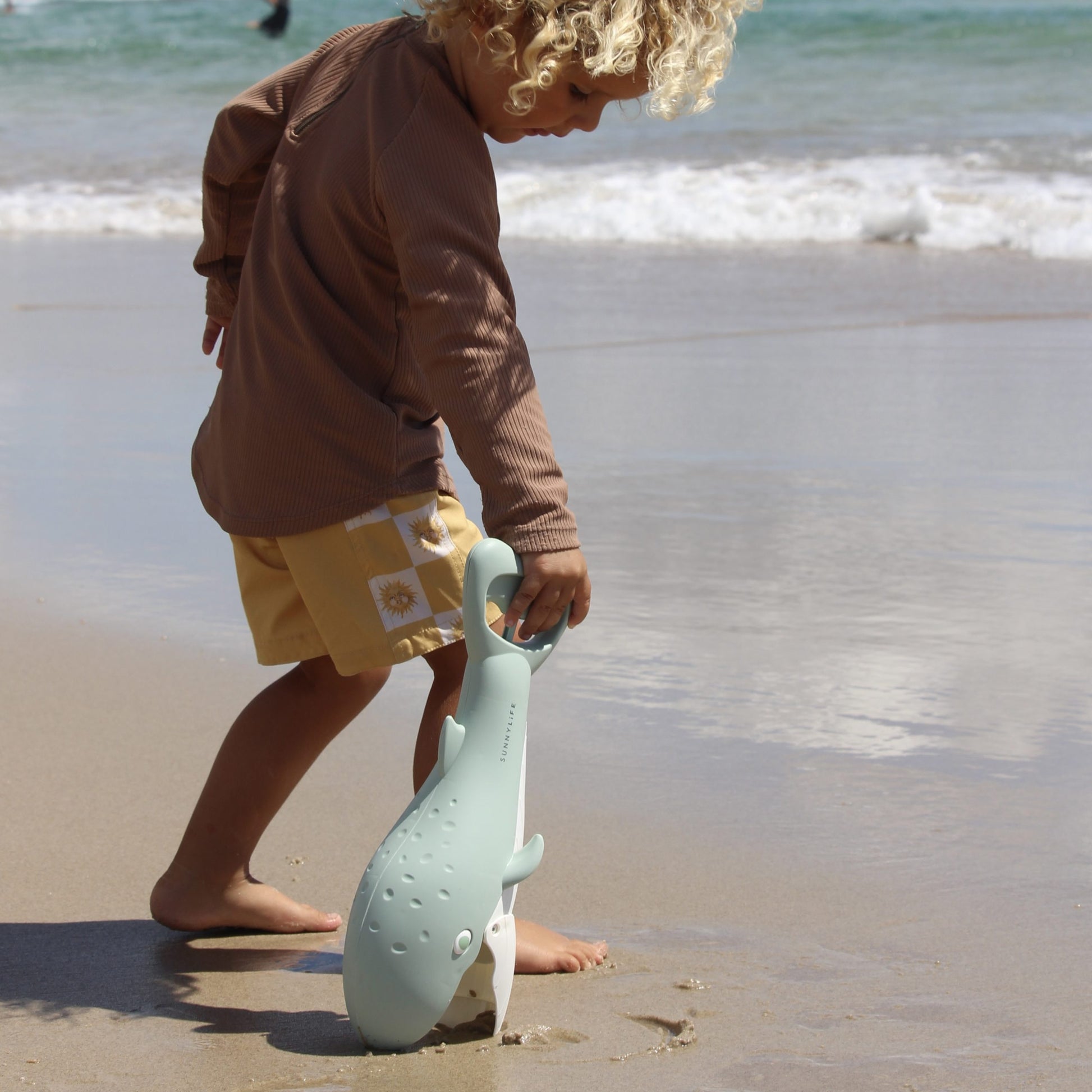 Łapki do piasku wieloryb marki LOQI trzymane przez dziecko na plaży przy morzu