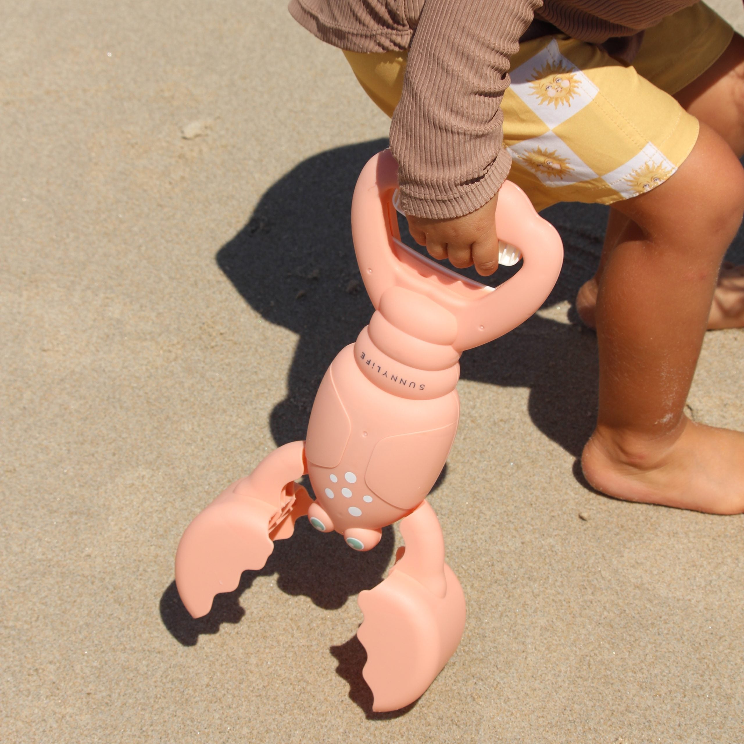 Łapki do piasku dla dzieci w kształcie kraba firmy LOQI trzymane przez dziecko na plaży