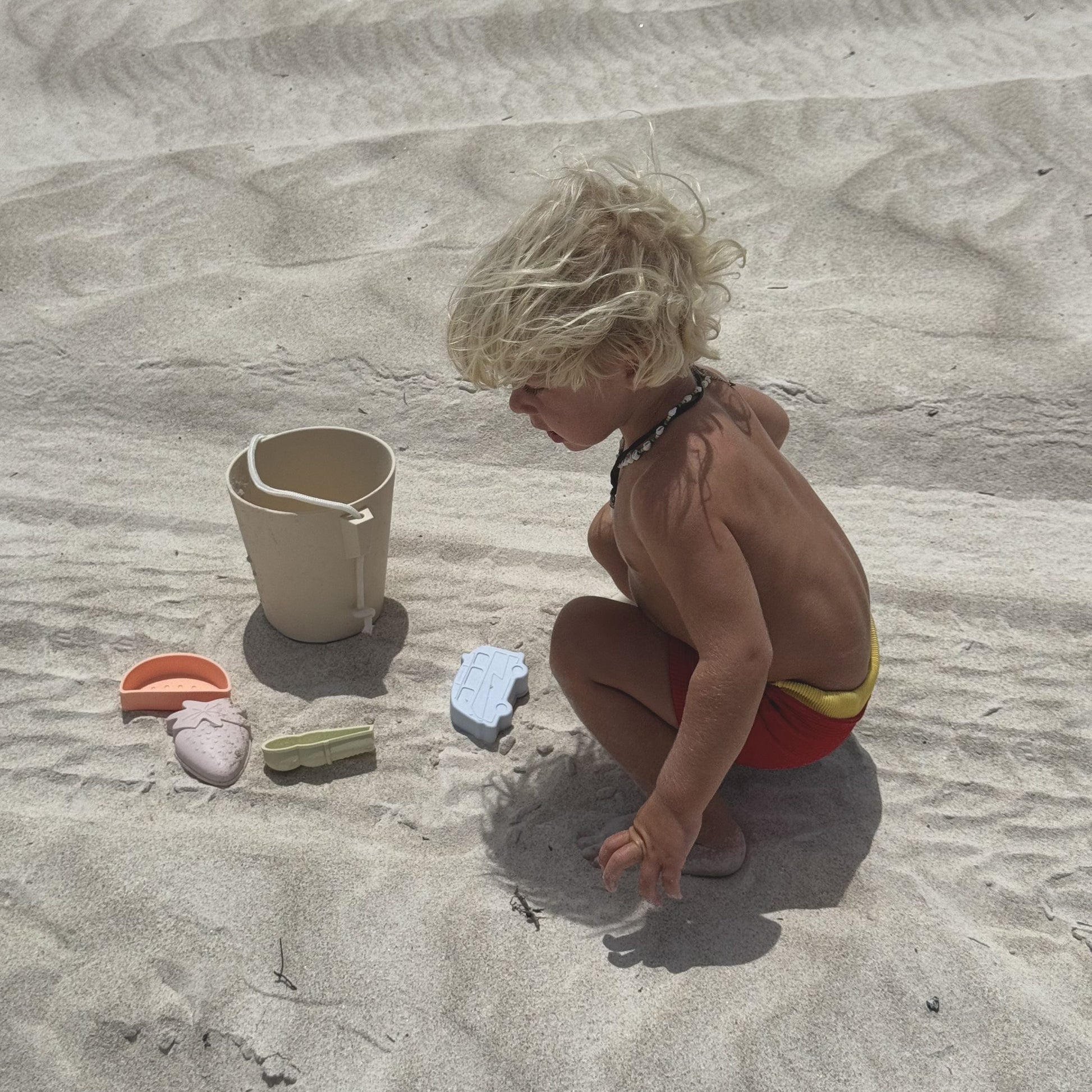 Dziecko bawiące się na piasku z silikonowe wiaderko dla dzieci marki Sunny Life i foremki do piasku