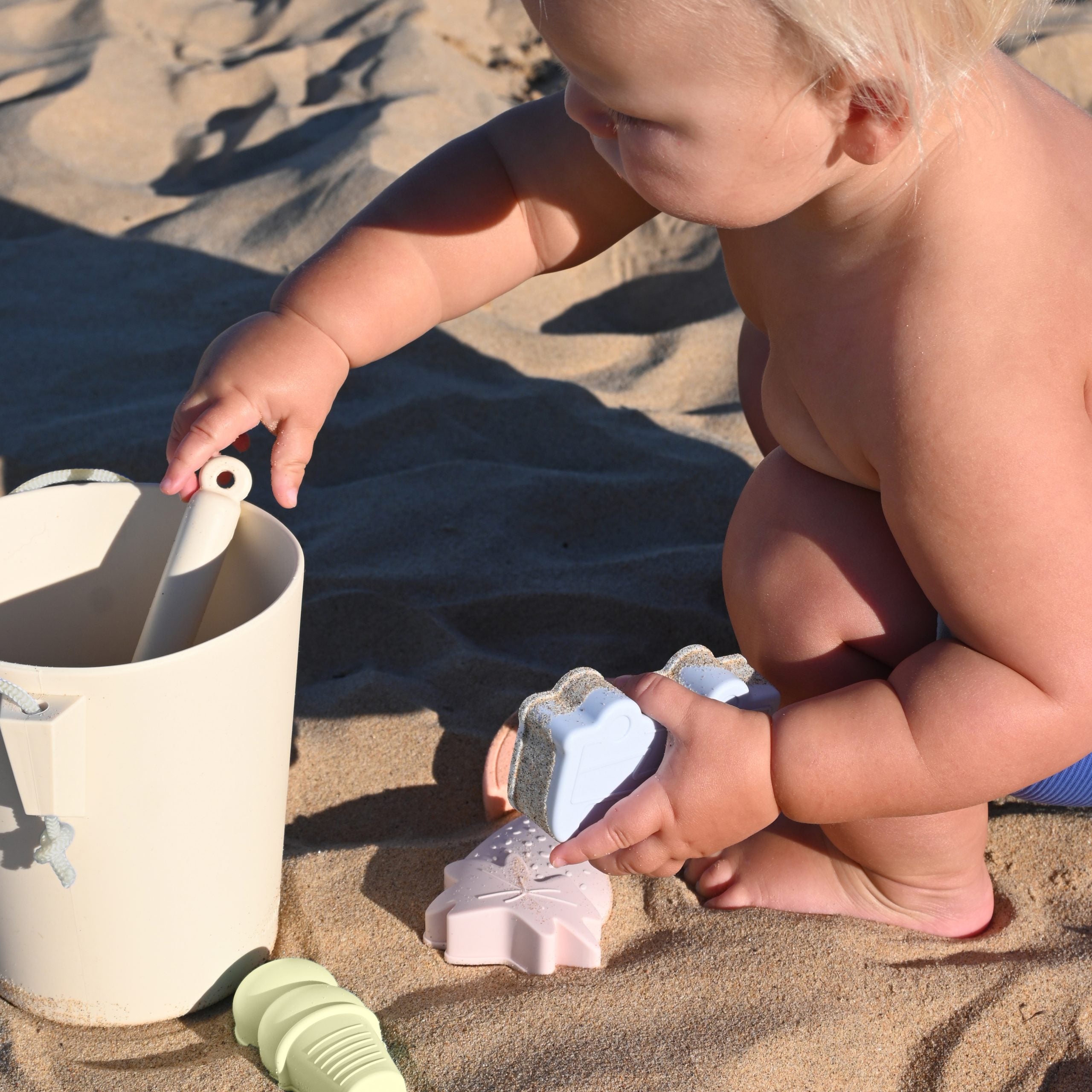 Dziecko bawiące się na plaży z silikonowe wiaderko dla dzieci marki Sunny Life na piasku