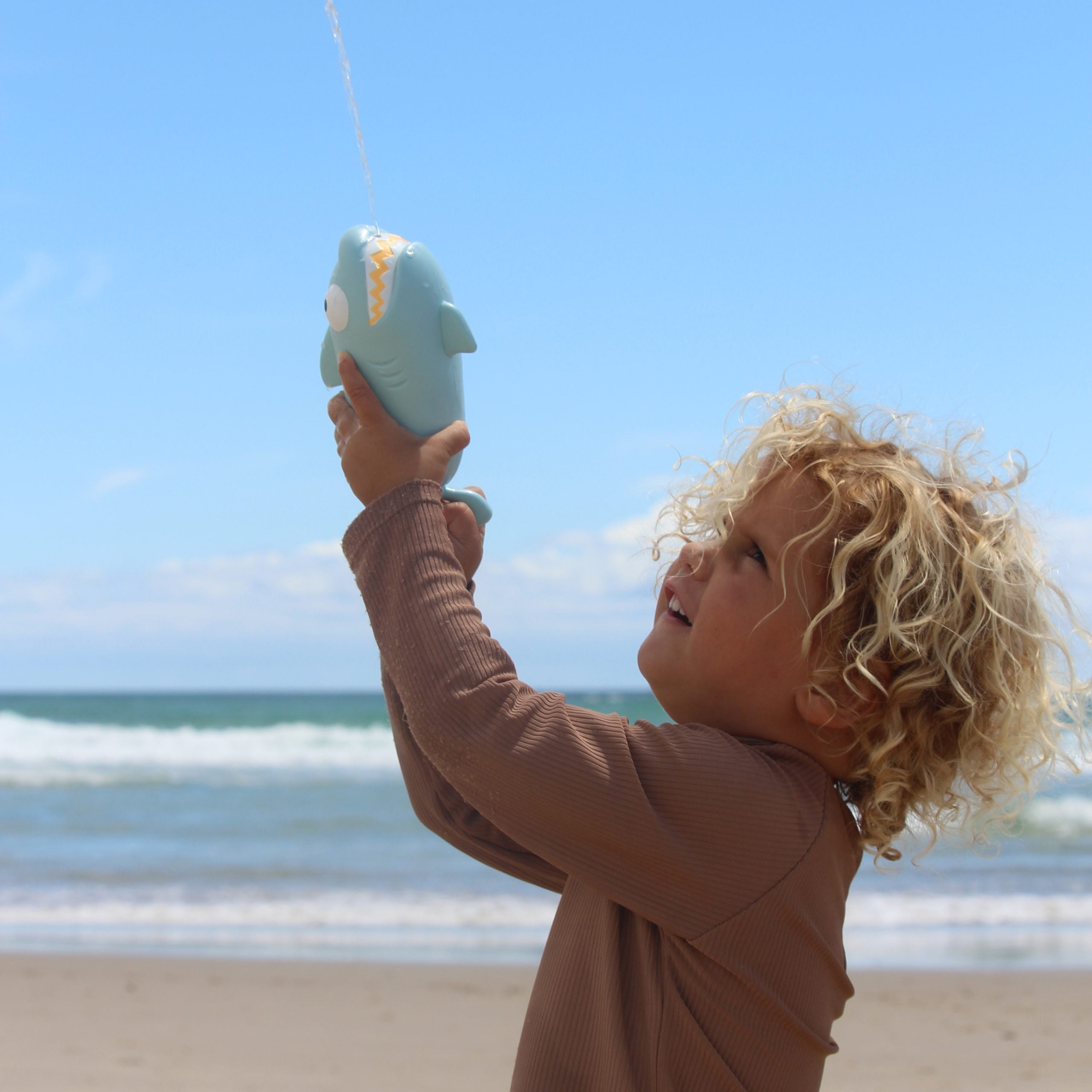 Dziecko bawiące się pistoletem wodnym rekin dla dzieci na plaży w słoneczny dzień